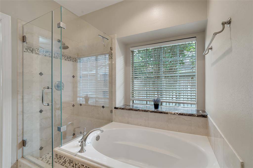 The primary bath has an updated frameless shower door. The tub has a brushed nickel faucet and decorative tile surround.