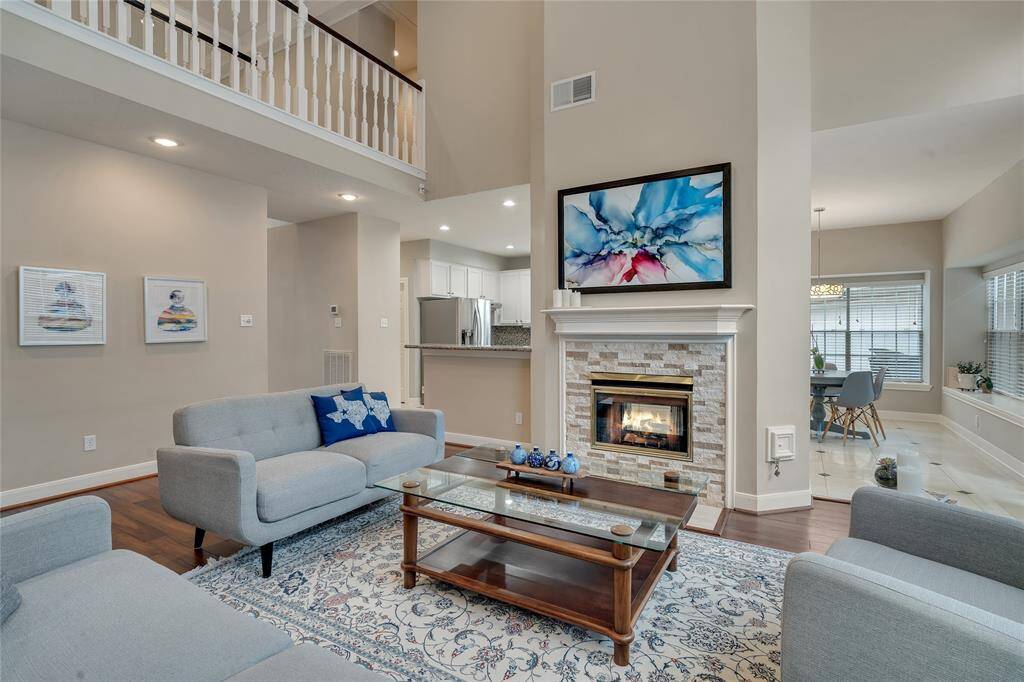 Another view of the living room with double-height ceilings and a cozy fireplace with stacked stone accent.