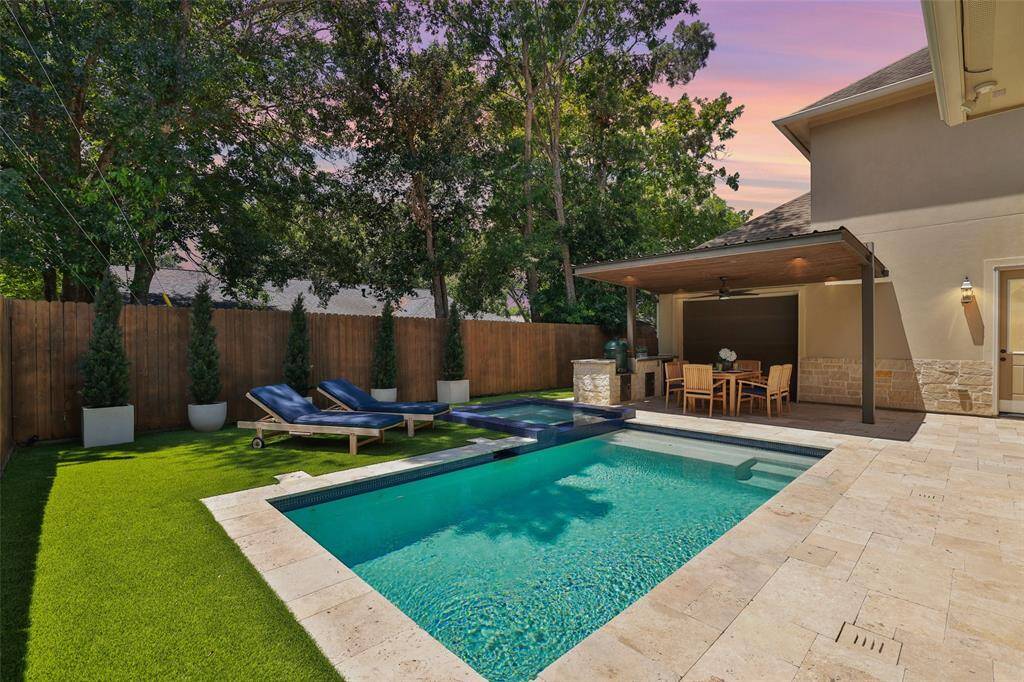 Discover a backyard paradise featuring a covered porch and elegant travertine pool deck, perfect for family fun.