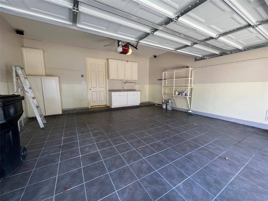 Fully tiled 2-car garage with storage cabinets and work space.