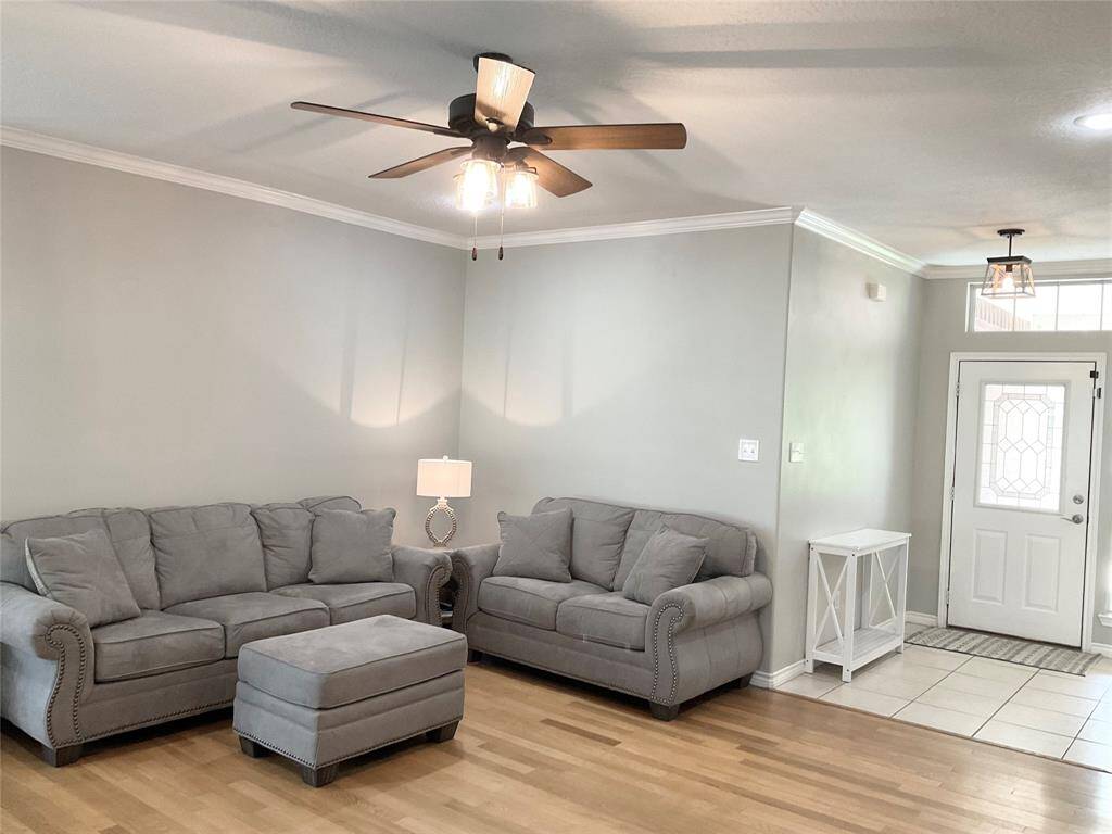 This inviting living room features light gray walls, wood flooring, and a ceiling fan. Plenty of room for a large  cozy sofa set and a matching ottoman. The entryway is tiled with a decorative glass door, and tile entry.  Walk right in and feel at home!