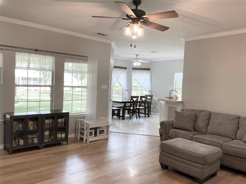 Bright, spacious open living area with hardwood floors, large windows, and ceiling fans. The space offers plenty of room for a cozy sectional sofa and an adjacent dining area with natural light.