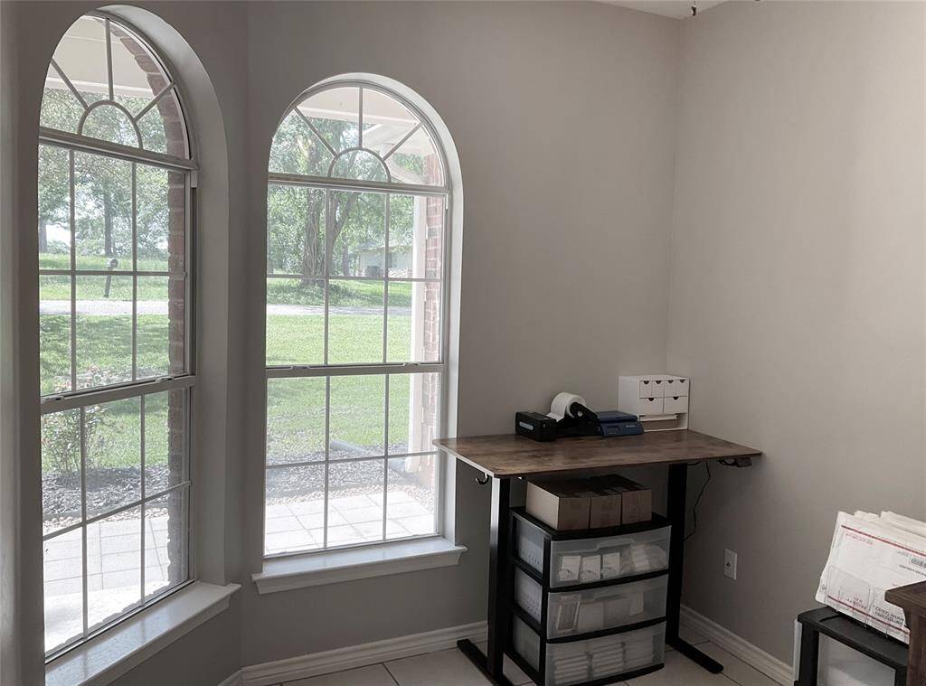 This room features three tall arched windows providing ample natural light and a view of the lush greenery outside. This room is ideal for a home office, play room, or a 4th bedroom with a full closet. The neutral wall color and tiled floor create a clean, modern feel.