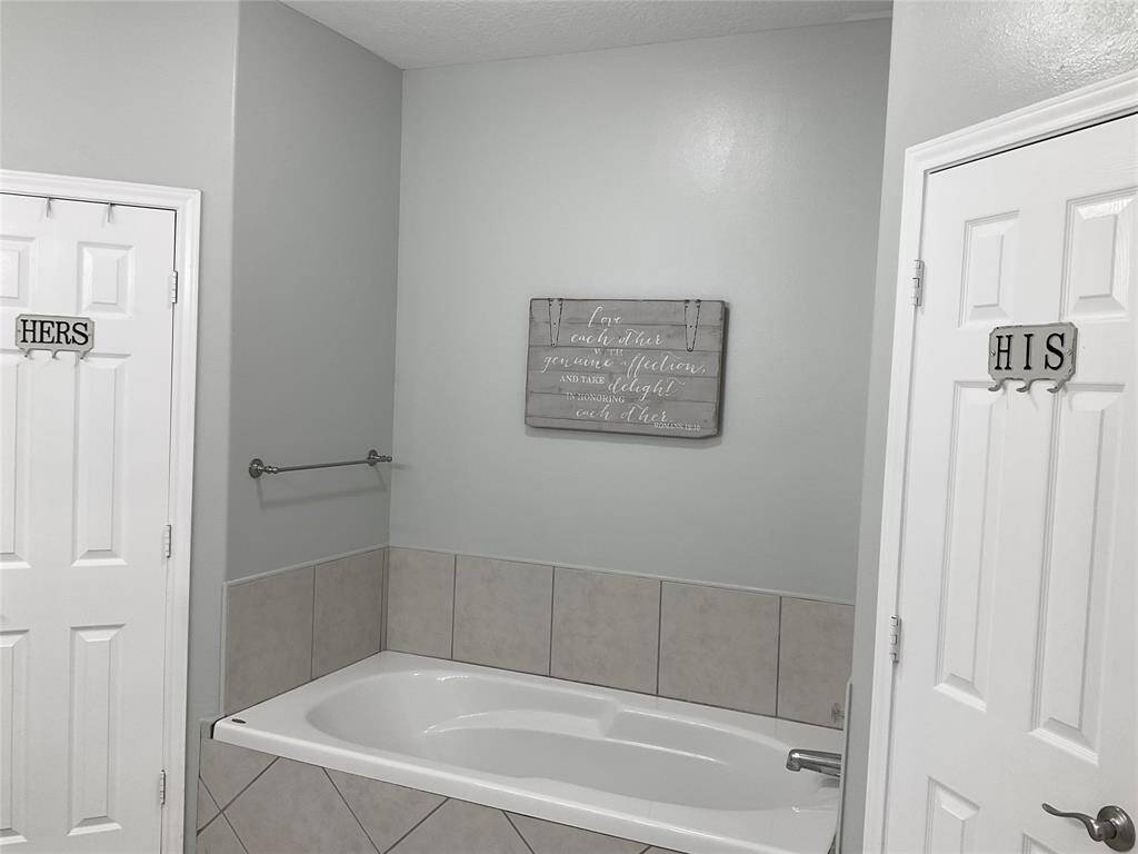 The primary bathroom is modernized with a sliging barn door, sink and fixtures. A door leads to a tiled bathtub area, and there's a glimpse into the adjoining primary bedroom. The color scheme is neutral and soothing.  The huge soaking tub and separate shower are delightful.  Don't miss the TWO closets in the bathroom!