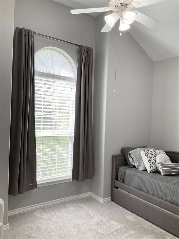 Bright, cozy room with a vaulted ceiling and a large arched window featuring elegant drapes. There's a modern ceiling fan, high ceilings, perfect for a bedroom or office space.