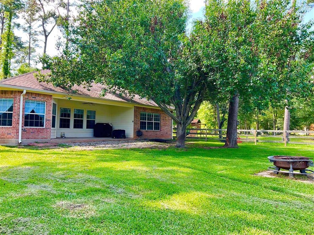 Spacious backyard with a well-maintained lawn and mature trees, featuring a cozy, 4 sided, brick house with large windows. The patio area is perfect for outdoor gatherings, and there's a fire pit for added enjoyment. A peaceful, inviting setting, in a hidden secret Lake front neighborhood, Cape Malibu.