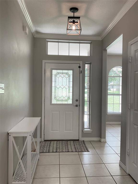 Bright entryway with a decorative glass front door, tile flooring, and a modern light fixture. The space includes a small console table and offers a view into the adjacent room with large windows. The room is an ideal home office or play room just off the living area.