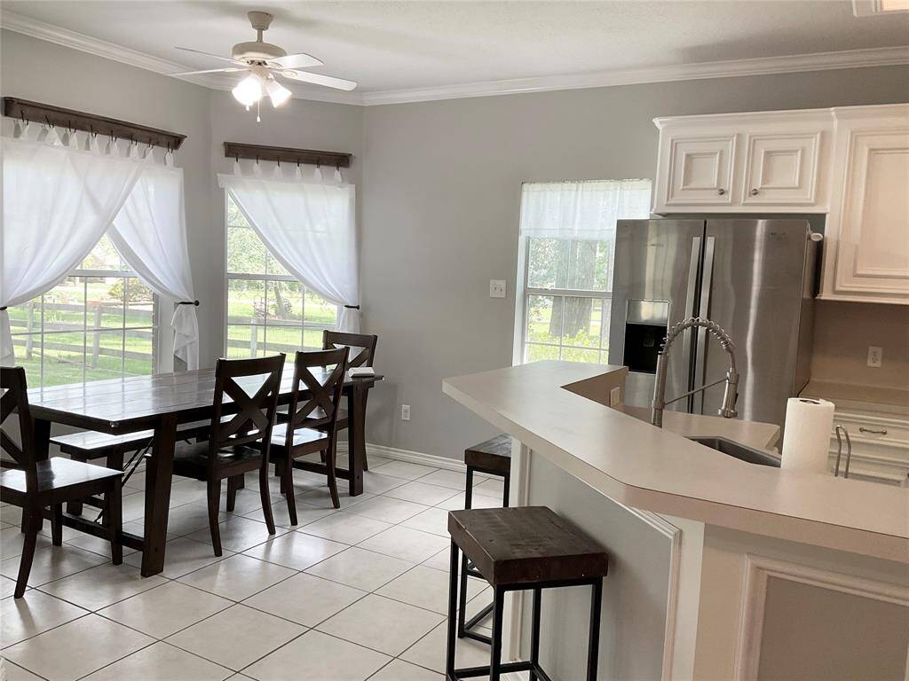 Bright kitchen and dining area with large windows, white cabinetry, and modern stainless steel appliances. Features a breakfast bar with seating and a ceiling fan for comfort. The family room is open to this living area and an ideal living space.