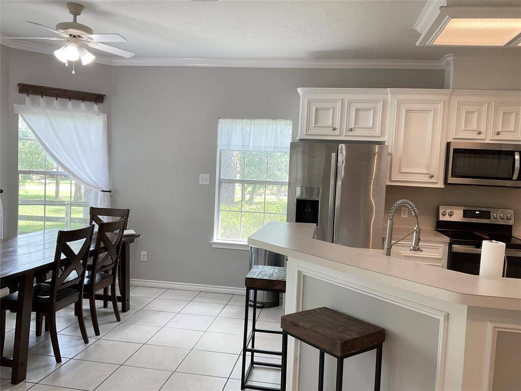 A bright kitchen and dining area features white cabinetry and modern stainless steel appliances. It includes a cozy dining nook with plenty of room for a large table, a ceiling fan, and large windows offering plenty of natural light.