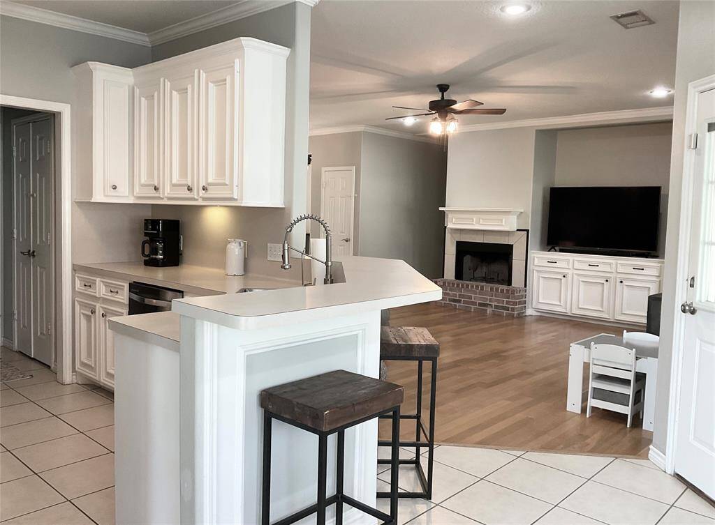 This home features a bright, open-concept living area with a modern kitchen, complete with white cabinetry and a breakfast bar. The cozy living room includes a real wood burning fireplace, ceiling fan, and built-in entertainment unit. Immediately it feels like Home Sweet Home!