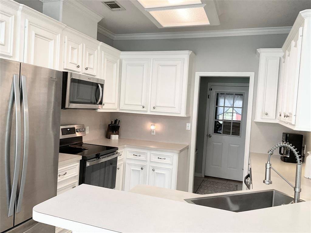 Modern kitchen with white cabinetry, stainless steel appliances, and sleek countertops. Features a large farmhouse sink with a flexible faucet, ample storage, and a door leading the  GARAGE GET AWAY WITH IT OWN 1/2 BATH, EPOXY FLOORING AND TV WALL MOUNT.