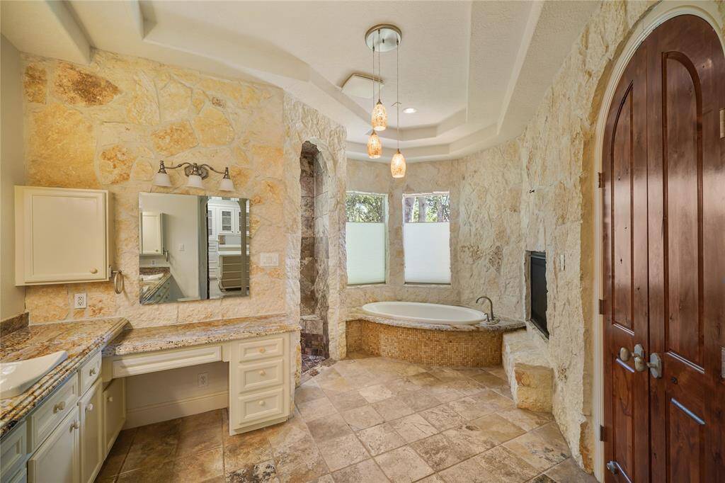 Spa- inspired primary bathroom showcasing a stunning stone see-through fireplace, soaking tub, open-concept walk-in shower with no glass, vanity, and double sinks - the ultimate blend of elegance, comfort, and design