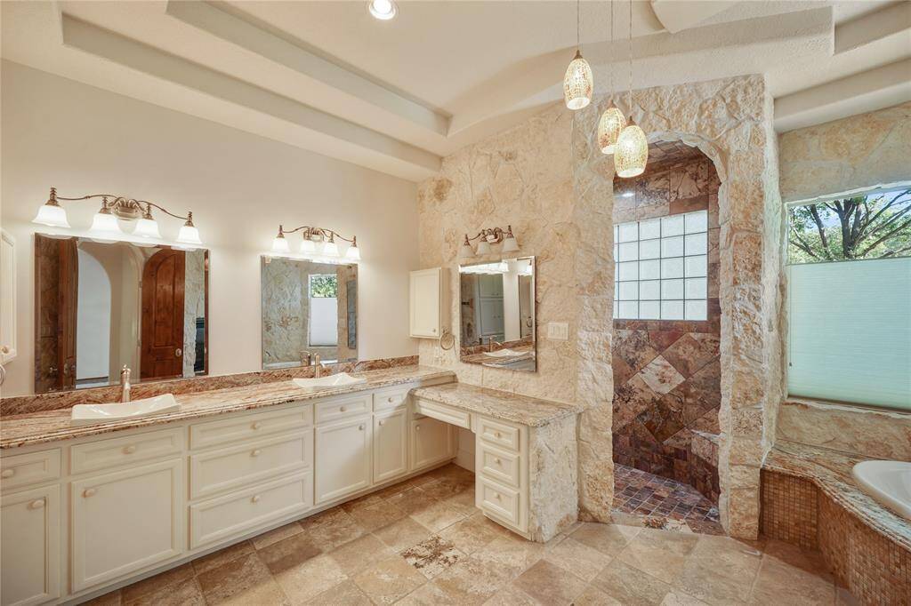 A fresh perspective on the primary bathroom highlights the seamless flow of natural stone, the soaking tub, and the spacious, open walk-in shower
