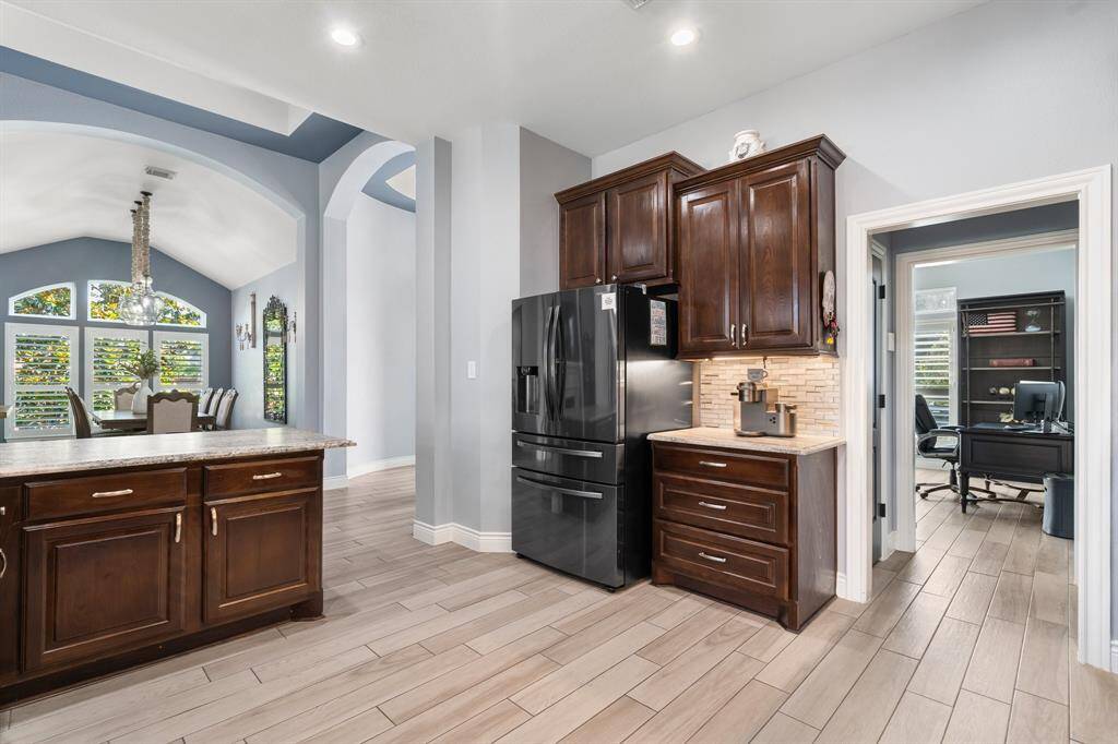 Experience modern elegance in this kitchen with wood cabinets, a sleek black fridge, and a stylish tiled backsplash. It seamlessly flows into a bright dining area with large windows and a chandelier.