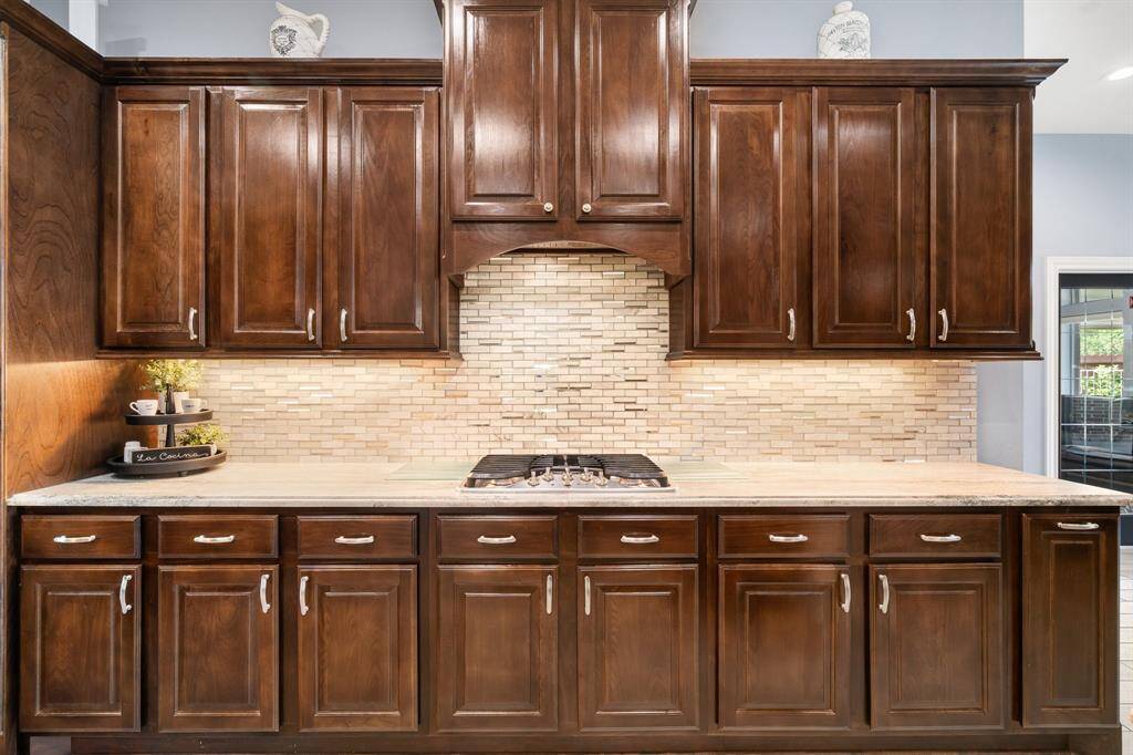 Discover a warm and functional kitchen with elegant wooden cabinets, generous storage, a chic tile backsplash, and a built-in stovetop.
