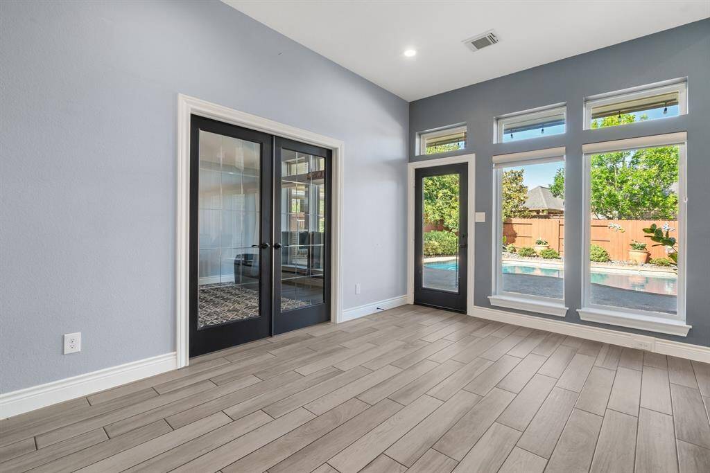 Bright room with large windows and glass doors opening to a pool area. Features light wood-look tile flooring and neutral walls for a modern, airy feel.