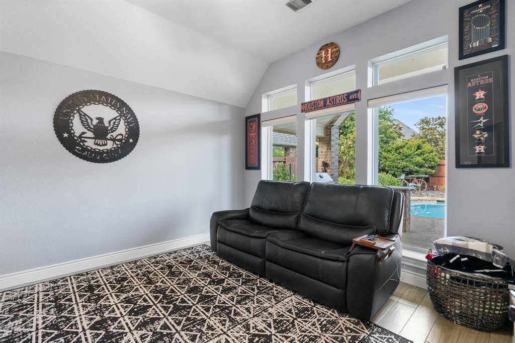 This room features a cozy, modern design with a black leather couch and a patterned rug. Large windows offer a view of a backyard pool, providing ample natural light. Decor includes sports memorabilia, adding a personal touch.