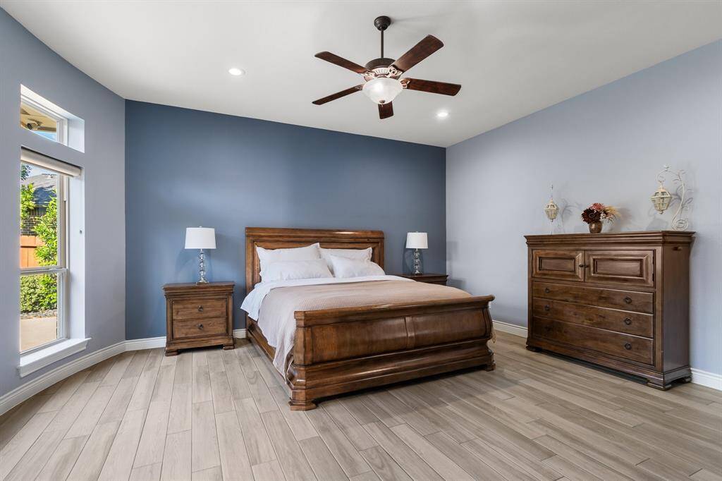 Discover relaxation in this cozy primary bedroom, featuring a stylish wooden bed and soft gray walls. Enjoy ample natural light, complemented by recessed lighting and a ceiling fan for the perfect ambiance.