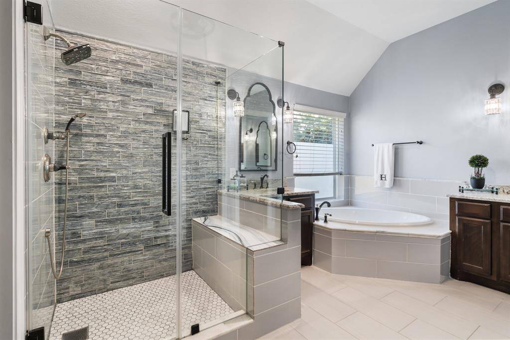 Experience luxury in this modern bathroom, featuring a sleek glass shower, a soaking tub, dual vanities, and stylish tile work, all illuminated by abundant natural light.
