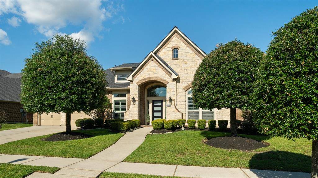 Featuring a well-maintained front yard with manicured shrubs and two symmetrical trees. The inviting walkway leads to a prominent front entrance, complemented by a spacious driveway.