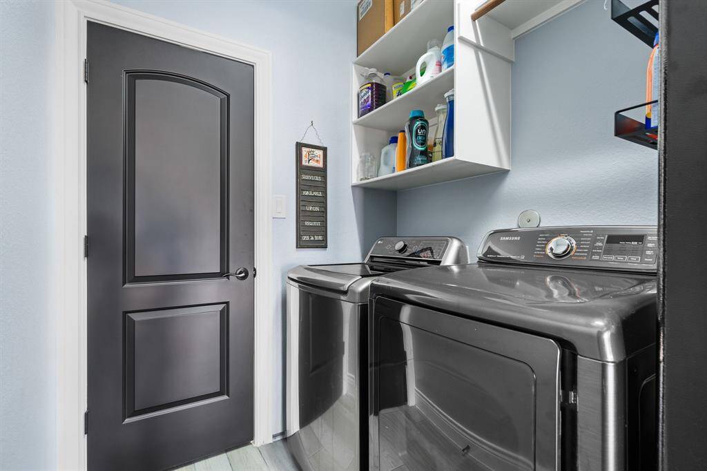 This photo features a compact, well-organized laundry room with modern black appliances, shelving for storage, and a sleek black door, offering functionality and style.