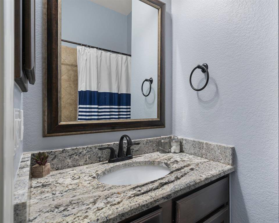 This bathroom features a sleek countertop with a stylish undermount sink. It has a large framed mirror, dark wood cabinetry, and a modern black faucet. A blue and white shower curtain adds a pop of color.