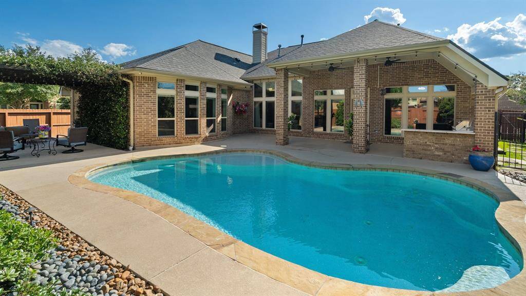 Discover a stunning backyard oasis featuring a modern pool and spacious patio. The brick home boasts large windows and a covered patio, ideal for dining and relaxation. Enjoy the beautifully landscaped area with a pergola-covered seating space, blending comfort and style effortlessly.