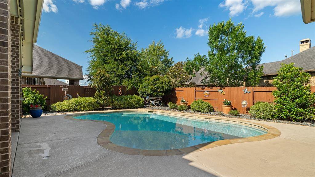 Discover a private oasis with a pristine swimming pool and spacious patio, bordered by a charming wooden fence and lush greenery. Perfect for relaxation and entertaining.