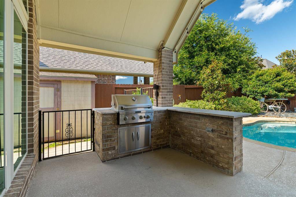 Experience the ultimate outdoor oasis with this cozy patio, featuring a covered brick grilling station next to a sparkling pool. Surrounded by lush landscaping and a wooden fence, it's perfect for entertaining.
