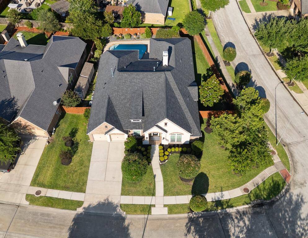 This aerial view showcases a spacious single-family home with a well-maintained yard and a private backyard pool. The property is located on a corner lot in a suburban neighborhood, offering ample driveway space and lush greenery.