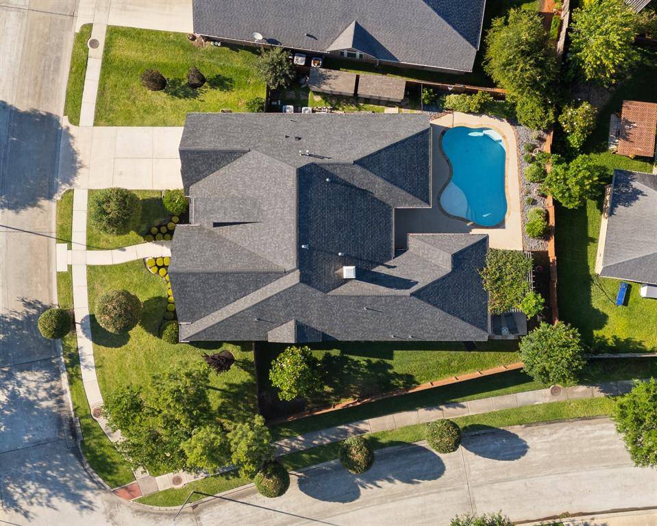 Discover this stunning home on a corner lot, featuring a modern multi-gabled roof and a uniquely shaped pool. Surrounded by a lush lawn and mature trees, it offers tranquility in a serene neighborhood.
