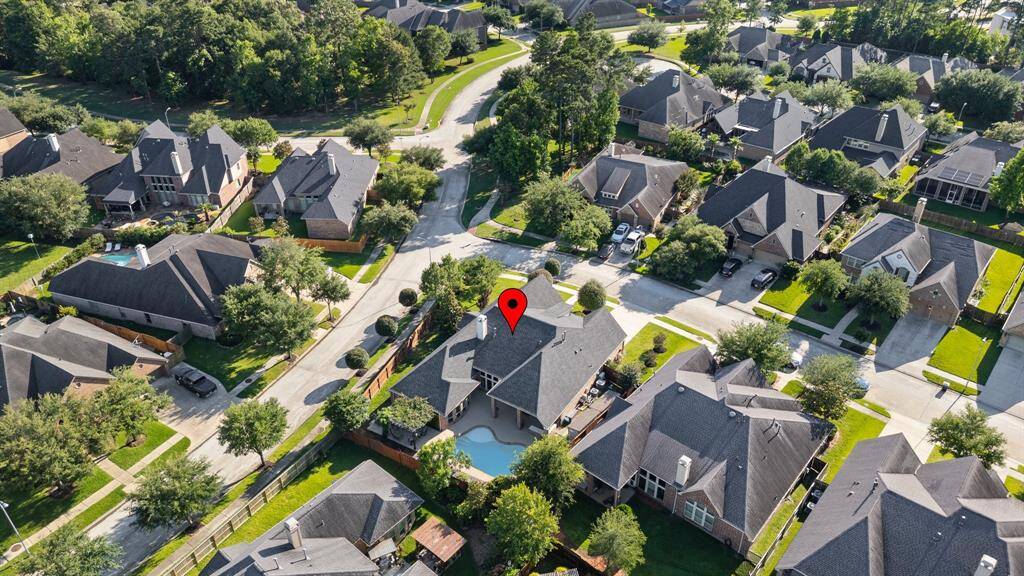This photo shows a suburban neighborhood with well-maintained homes, mature trees, and green lawns. The highlighted house has a backyard pool and is situated on a quiet, curved street.