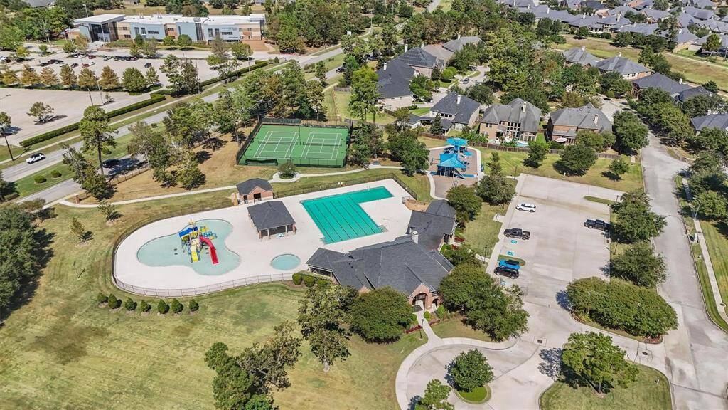 Neighborhood aerial photo showcases a vibrant community area featuring a large swimming pool, a children's splash pad, tennis courts, and a playground. The surrounding neighborhood is lush with greenery and well-maintained homes, offering a welcoming and active environment for residents.