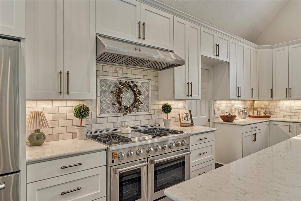 Kitchen features modern white cabinetry, a stylish Carrara marble backsplash, and a stainless steel gas range with sleek hood. Ample countertop space and under-cabinet lighting.
