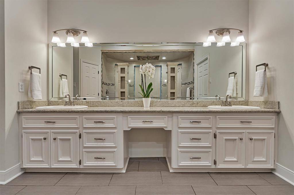 Primary bathroom with a dual-sink vanity. Granite countertops, ample cabinet storage, large mirrors, and modern light fixtures, offering a bright and functional space.