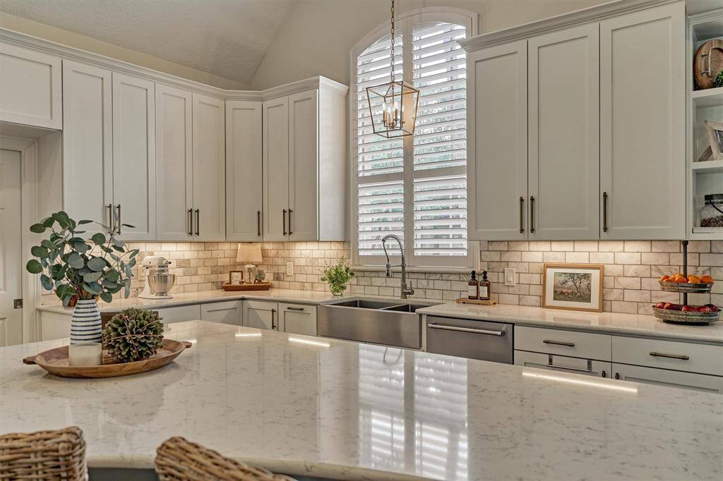 Kitchen boasts a spacious, bright layout with modern white cabinetry, quartz countertops, and a large island. Stainless steel appliances, farmhouse sink, and elegant lighting.