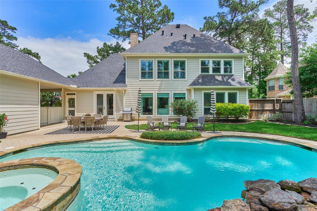 Spacious backyard with a beautiful pool and spa, perfect for relaxation and entertaining. The patio area includes outdoor seating and dining space, surrounded by lush greenery.