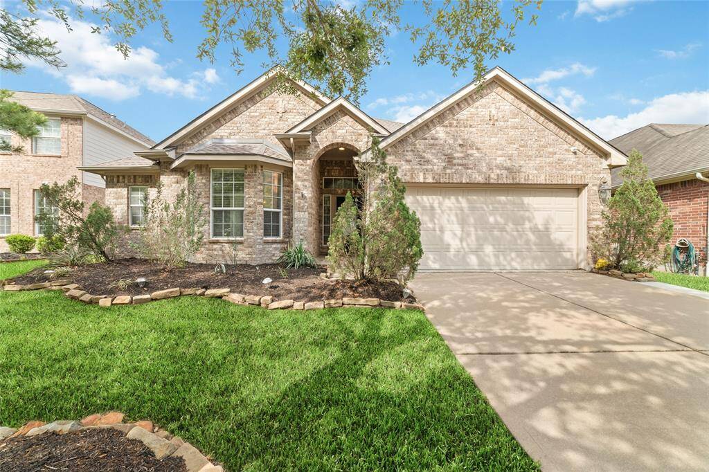 This charming brick home features a welcoming front with a well-maintained lawn, landscaped garden beds, and a two-car garage. The arched entryway and large windows add to its curb appeal, creating a warm and inviting atmosphere.