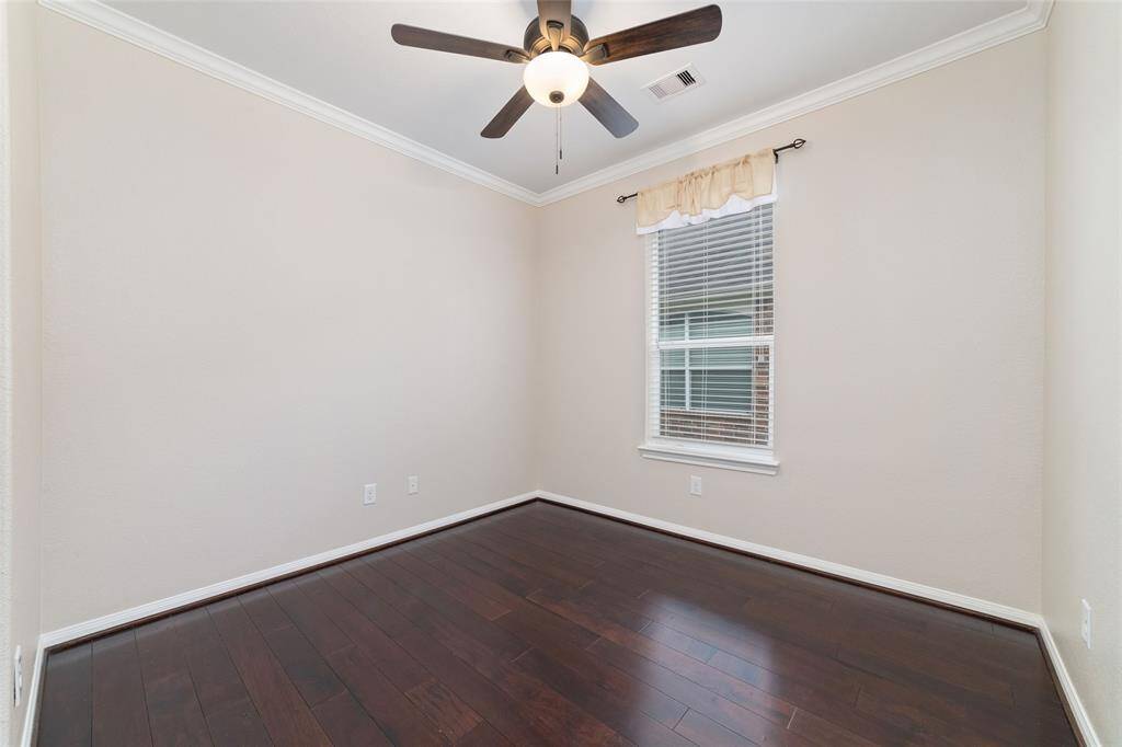 This room features dark floors, neutral walls, and a ceiling fan with a light. A window with blinds and a valance provides natural light. It's a versatile, cozy space perfect for a smaller bedroom or office.