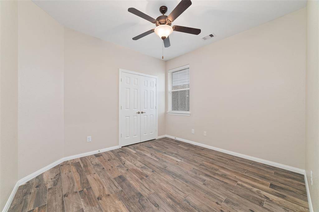 This room features neutral walls, wood-like flooring, a ceiling fan, and ample natural light from a window. It also includes a double-door closet, making it versatile for various uses.
