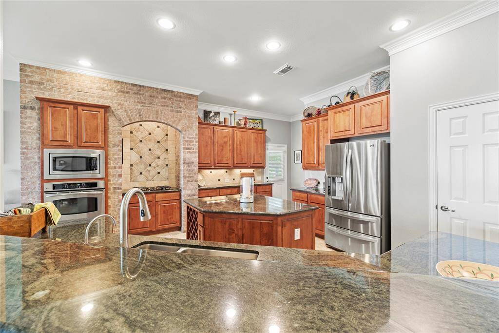 This spacious kitchen boasts wood cabinetry, a center island, cooktop, dishwasher, disposal, microwave, ample counter space, and abundant cabinet storage.