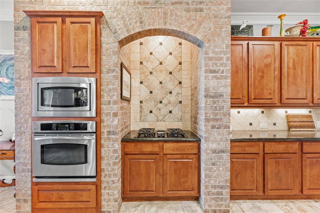 Alternate view of the kitchen showcasing a separate cooktop, built-in stainless-steel oven and microwave, and rich wooden cabinetry.