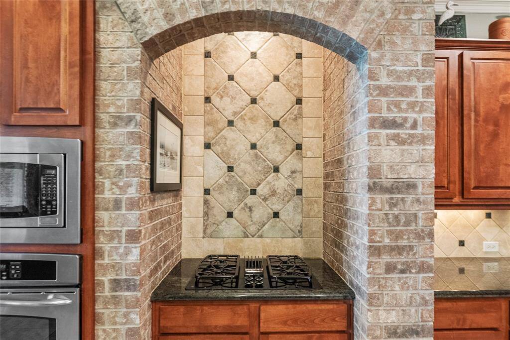 Close up view of the gas cooktop with brick all accent and decorative tile and travertine back splash.