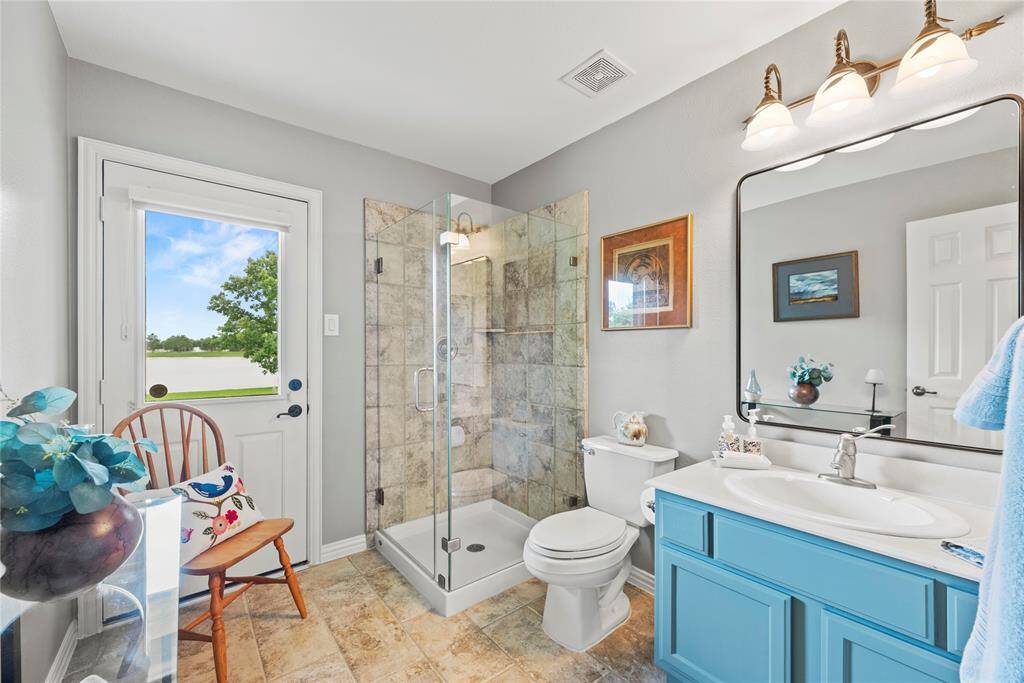 Bathroom # 3 with a door to the exterior patio.  Great for a future pool bath.  Features a glass-enclosed shower, vanity, sink, large mirror, and tile flooring.
