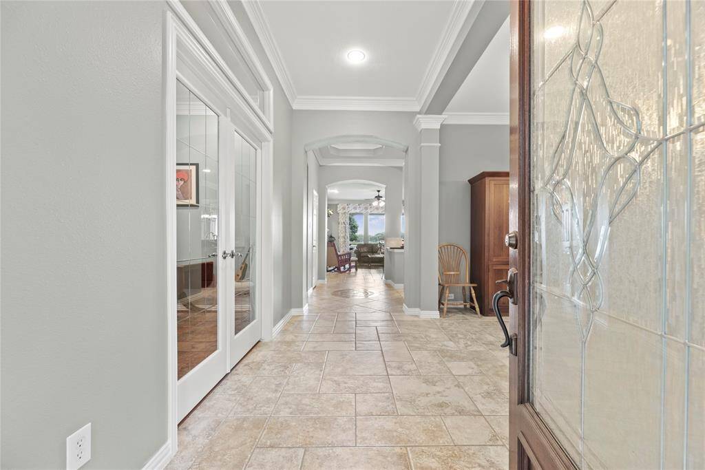 Bright entryway with tile flooring, crown molding, and hallway that opens up to a spacious family room.