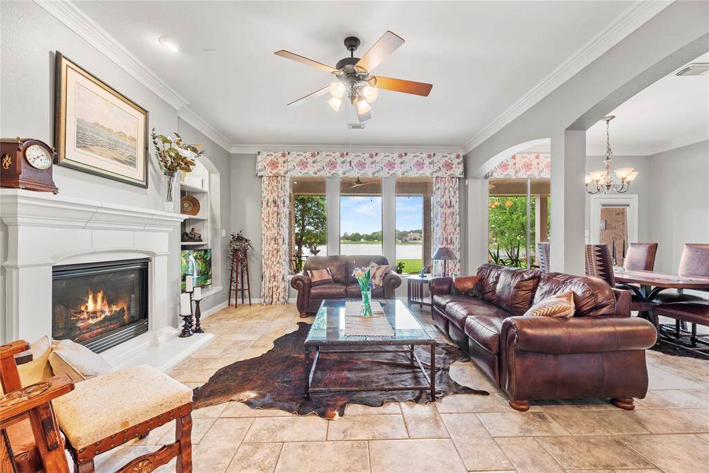 This spacious family room features a gas fireplace, tile flooring, and large windows offering scenic views. The open layout connects to a breakfast area and is open to the kitchen.