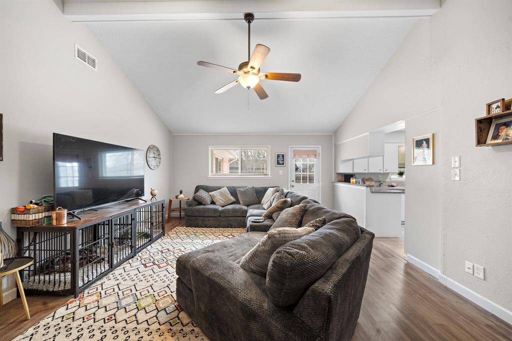This inviting living room features high ceilings with a ceiling fan. An open layout connects to the kitchen, creating a seamless flow.