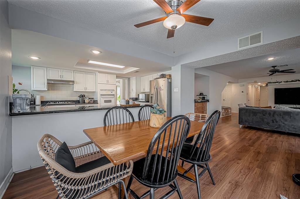 This open-concept space features a modern kitchen with white cabinets, stainless steel appliances, and a granite countertop that extends to a cozy dining area. The adjacent living room offers ample space with wood flooring and ceiling fans, creating a comfortable and inviting atmosphere.