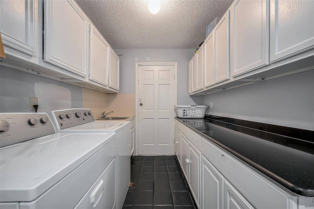 This photo shows a spacious laundry room with ample cabinetry and countertop space. It features a washer and dryer, a utility sink, and a tiled floor, offering practicality and storage for household needs.
