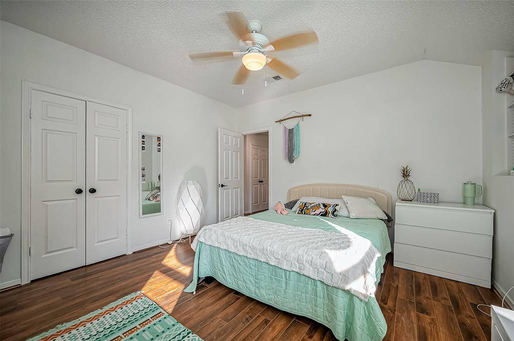 Bright and cozy bedroom with wood flooring, featuring a ceiling fan, ample closet space, and modern decor. The room includes a comfortable bed, a dresser, and a small wall shelf, creating a welcoming atmosphere.